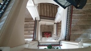 Un magnifique escalier avec une rampe en bois, un mur de marbre et une œuvre d’art encadrée au bas de l’escalier.
