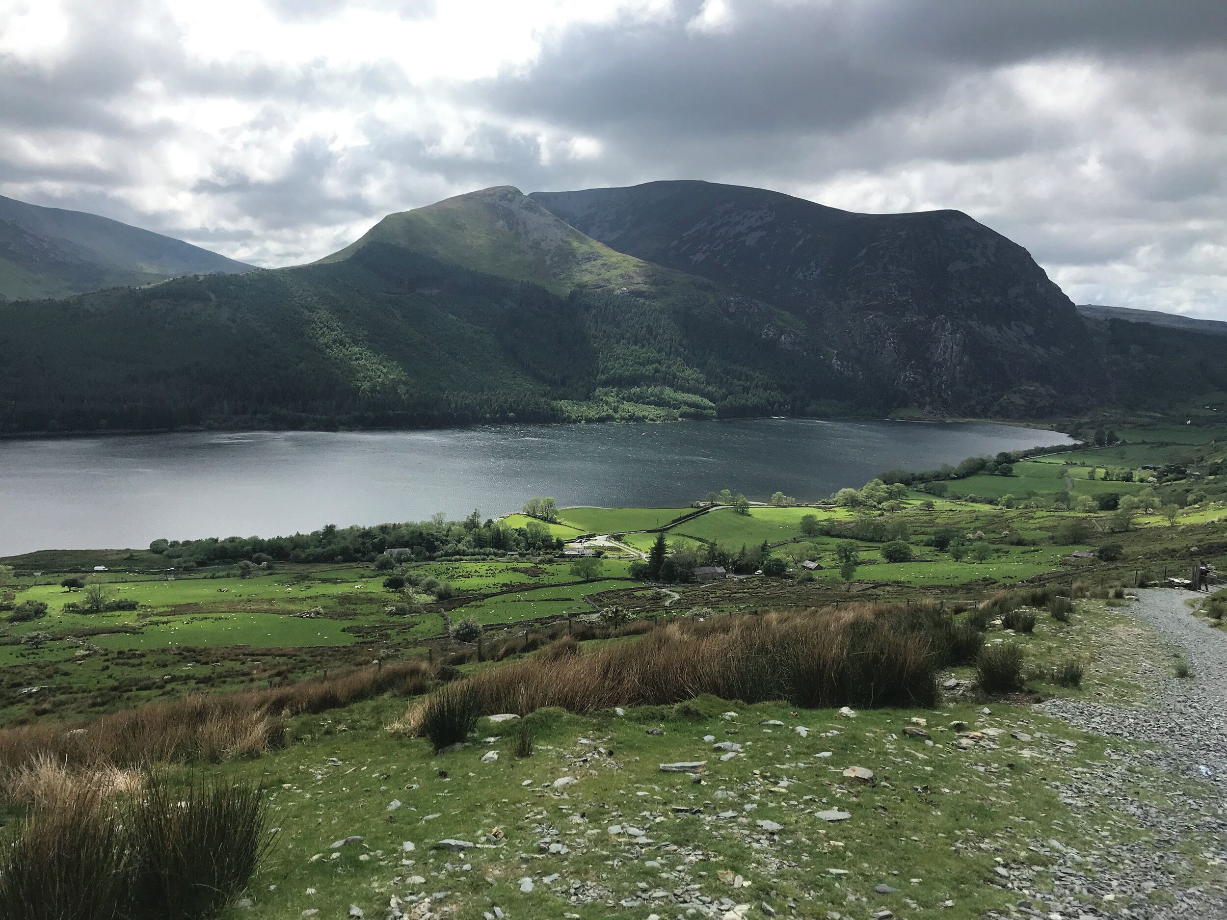 Un paysage montagneux avec un lac, des champs verdoyants et quelques bâtiments dispersés.