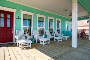 A covered porch with white Adirondack chairs, a red door, and teal siding. - The Lazy Lobster 3 Bedroom Home by RedAwning (Port Bolivar)