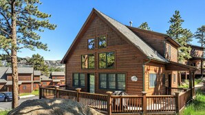 A wooden cabin with a balcony, large windows, and a view of the surrounding forest.