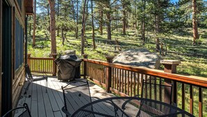 A wooden deck with outdoor furniture, a barbecue grill, and a view of a forested area.