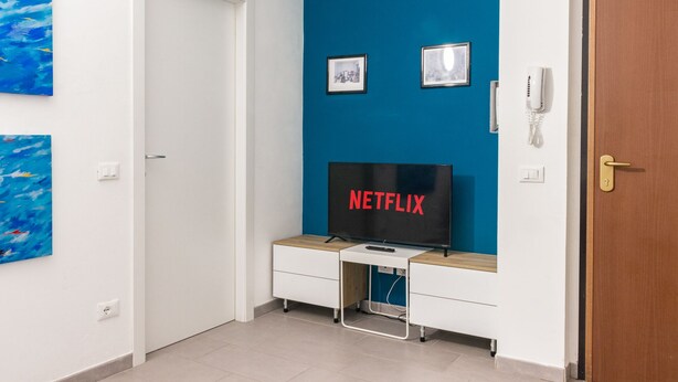 A room with a blue accent wall, a white door, and a desk with a television displaying "NETFLIX".