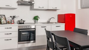 A modern kitchen with white cabinets, a stainless steel range, a red refrigerator, and a dining area with a table and chairs.