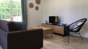 A modern living room with a sofa, a wooden coffee table, a TV on a wooden stand, a black chair, and a window with curtains.