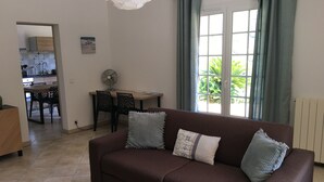 A living room with a brown sofa, two black chairs, a wooden table, and a fan.