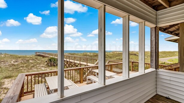 A covered outdoor deck with a view of the beach and dunes.