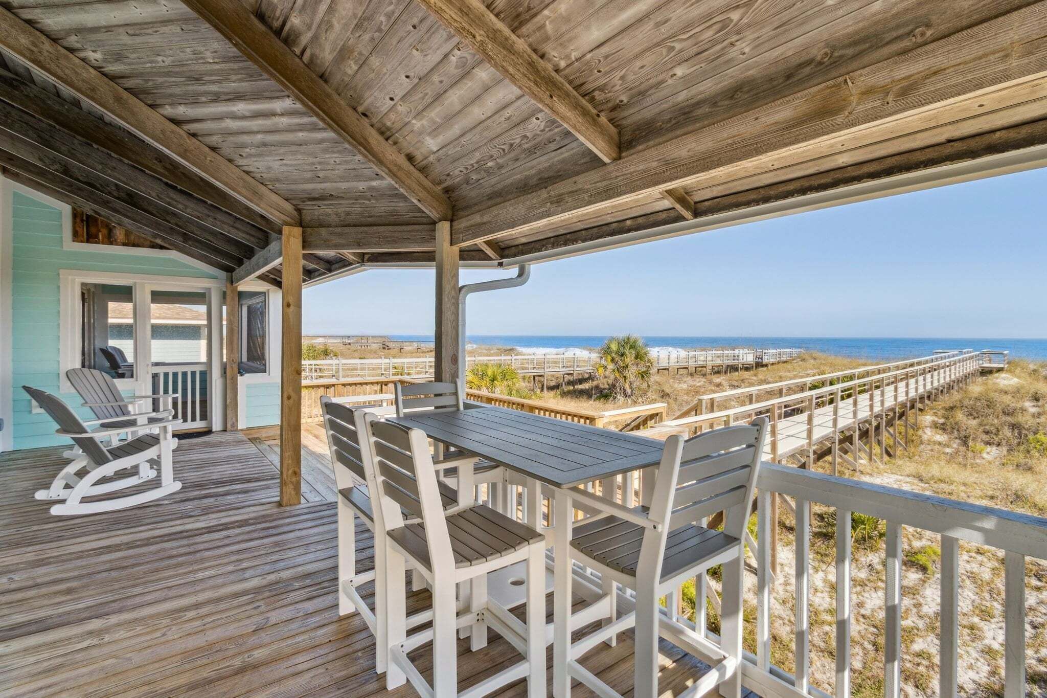 A wooden deck with a covered area, white rocking chairs, and a table with chairs.