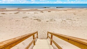 A beach with wooden stairs leading to the water, sandy beach, and a clear blue sky.