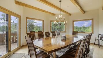 A spacious dining area with a large wooden table and chairs, large windows with a view, and a chandelier.