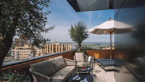 A rooftop terrace with a sofa, chairs, a table, and an umbrella.