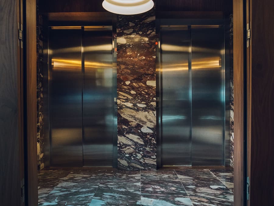 Un ascensor con una columna de mármol, paredes de madera y una lámpara moderna.