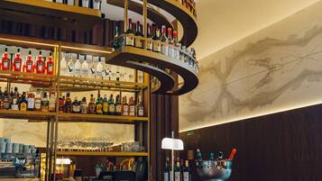 Uma área de bar com várias prateleiras de garrafas de bebidas, banquetas e teto decorativo.