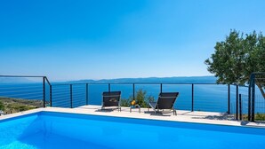 A pool with two chairs and a table, overlooking a clear blue sea and distant mountains. - Villa Mountain Lodge (Lokva Rogoznica)