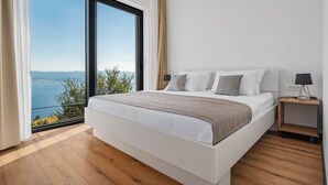 A modern bedroom with a large bed, a nightstand, and a view of the sea. - Villa Mountain Lodge (Lokva Rogoznica)
