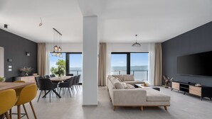 A modern living room with a large TV, a sofa, and a dining area with chairs and a table. - Villa Mountain Lodge (Lokva Rogoznica)