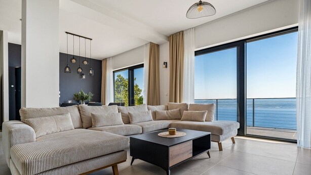 A modern living room with a large sectional sofa, a coffee table, and a view of the sea through large windows. - Villa Mountain Lodge (Lokva Rogoznica)