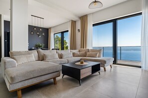 Ein modernes Wohnzimmer mit einem großen Ecksofa, einem Couchtisch und Meerblick durch große Fenster.