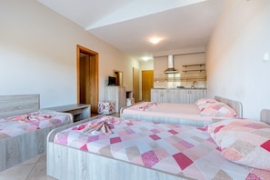 A hotel room with two beds, a desk, a chair, a kitchenette, and a bathroom.