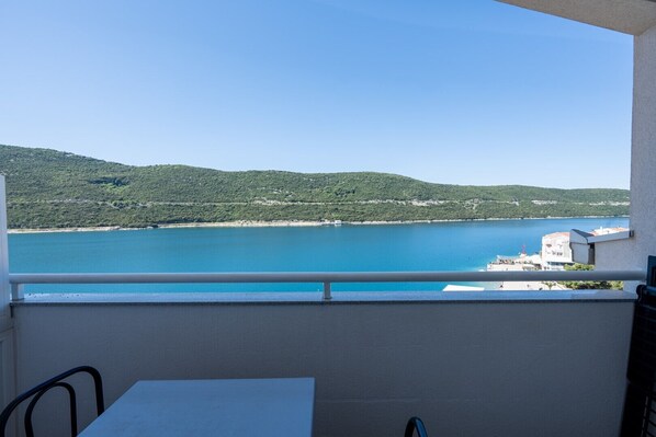 A balcony with a view of a calm sea and green hills.