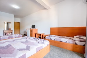 A hotel room with two beds, a desk, a mirror, a wardrobe, and a small refrigerator.