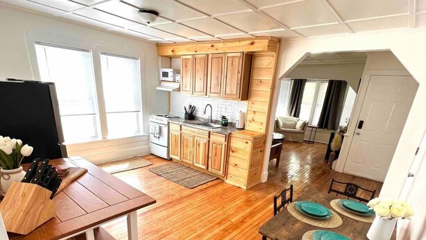 Una cocina moderna con armarios de madera, microondas integrado y comedor con mesa y sillas de madera.