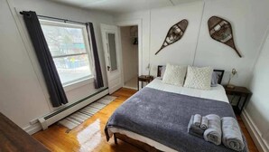 Un dormitorio con cama, mesita de noche, ventana con cortinas y un adorno en la pared.