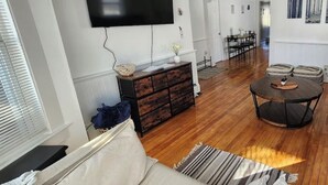 Una sala moderna con un televisor de pantalla plana montado en la pared, una mesa de comedor de madera y un sofá con una manta.
