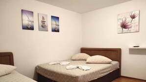A neatly arranged bedroom with a large bed, two smaller beds, and three wall-mounted artworks depicting boats and flowers. - Apartmani Kata / Studio apartment 3 on the ground floor (Neum)