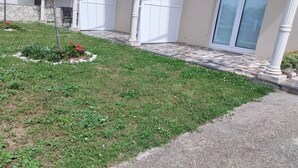 A residential building with a paved driveway, a small garden with red flowers, and a white garage door.