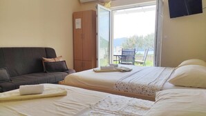 A bedroom with two beds, a sofa, and a view of a balcony with a table and chairs.