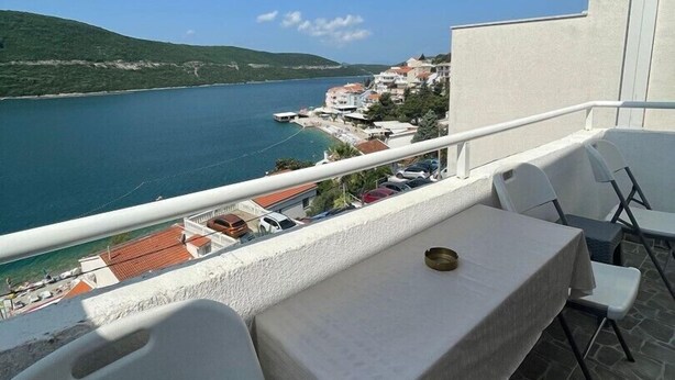 A balcony with a table and chairs overlooking a coastal town and sea.