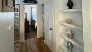 A hallway with a white door, a shelf with decorative items, and a sign above the door.