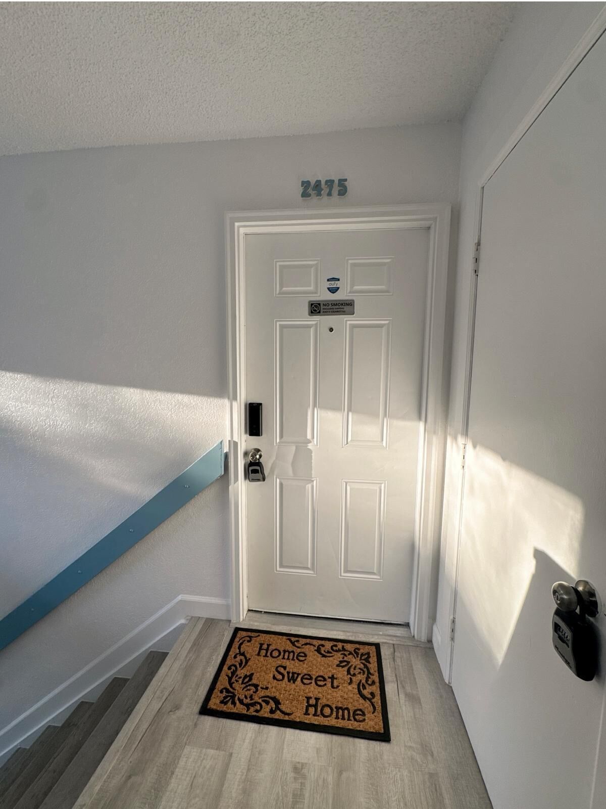 A white door with a 'NO SMOKING' sign, a mailbox, and a doormat with 'Home Sweet Home' text.