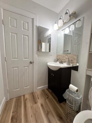 Un baño con puerta blanca, lavamanos con espejo y retrete.