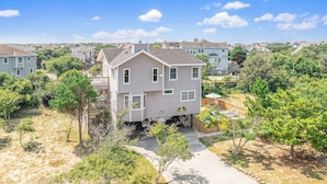 A two-story house with a covered patio and a small deck, surrounded by trees and a clear sky. - Unforgettable! Saltwater Pool! Newly Renovated! Walk to Beach, D0131 (Duck)