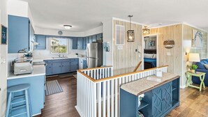 A modern kitchen with blue cabinets, a central island, and a wooden railing. - Unforgettable! Saltwater Pool! Newly Renovated! Walk to Beach, D0131 (Duck)