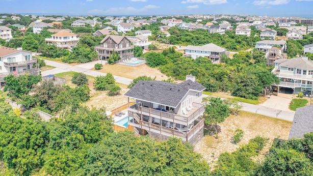 A residential area with multiple houses, a large house with a balcony and a swimming pool, surrounded by greenery. - Unforgettable! Saltwater Pool! Newly Renovated! Walk to Beach, D0131 (Duck)