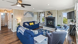 A living room with a blue sofa, a white coffee table, a fireplace, and a ceiling fan. - Unforgettable! Saltwater Pool! Newly Renovated! Walk to Beach, D0131 (Duck)