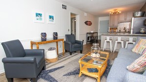 A living room with a sofa, two armchairs, a coffee table, and a dining area with bar stools. - Happy Waves-Oceanfront Condo! Sleeps 7! Tons of amenities! (Atlantic Beach)