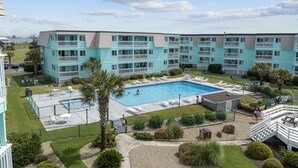 A multi-story building with a swimming pool, outdoor seating, and a fenced patio area. - Happy Waves-Oceanfront Condo! Sleeps 7! Tons of amenities! (Atlantic Beach)