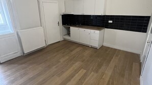 Une petite cuisine propre, avec des meubles blancs, un plan de travail noir et un revêtement de sol en bois.