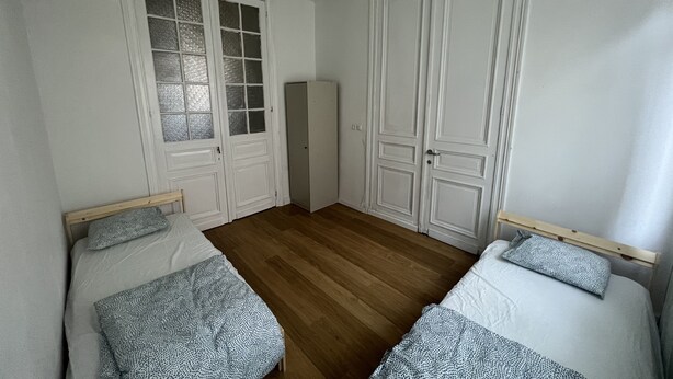 Une chambre avec deux lits simples, un plancher en bois, des murs blancs et des portes blanches dotées de panneaux de verre.