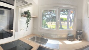 A compact kitchen with a sink, a toaster, a coffee maker, and a small window with a view of trees.