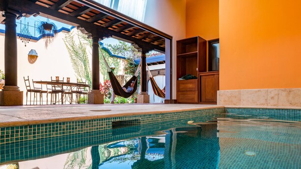 Une piscine avec un revêtement de sol en carrelage, un hamac et du mobilier d’extérieur.