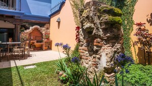 Une cour avec une fontaine en pierre, des sièges en plein air et une cheminée en briques.