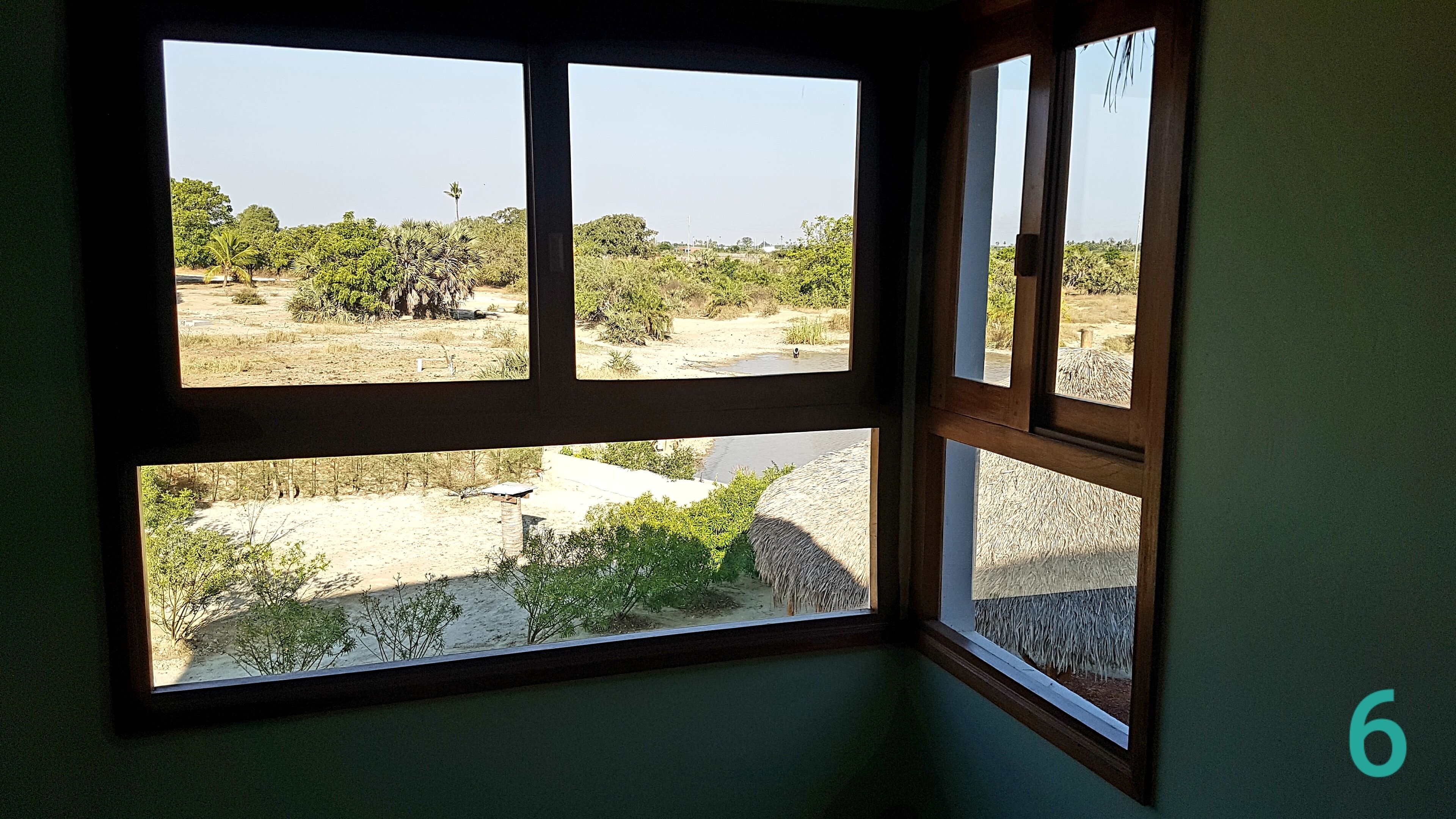 Een kamer met een groot raam dat uitzicht biedt op een droog landschap met schaarse begroeiing en enkele bomen.