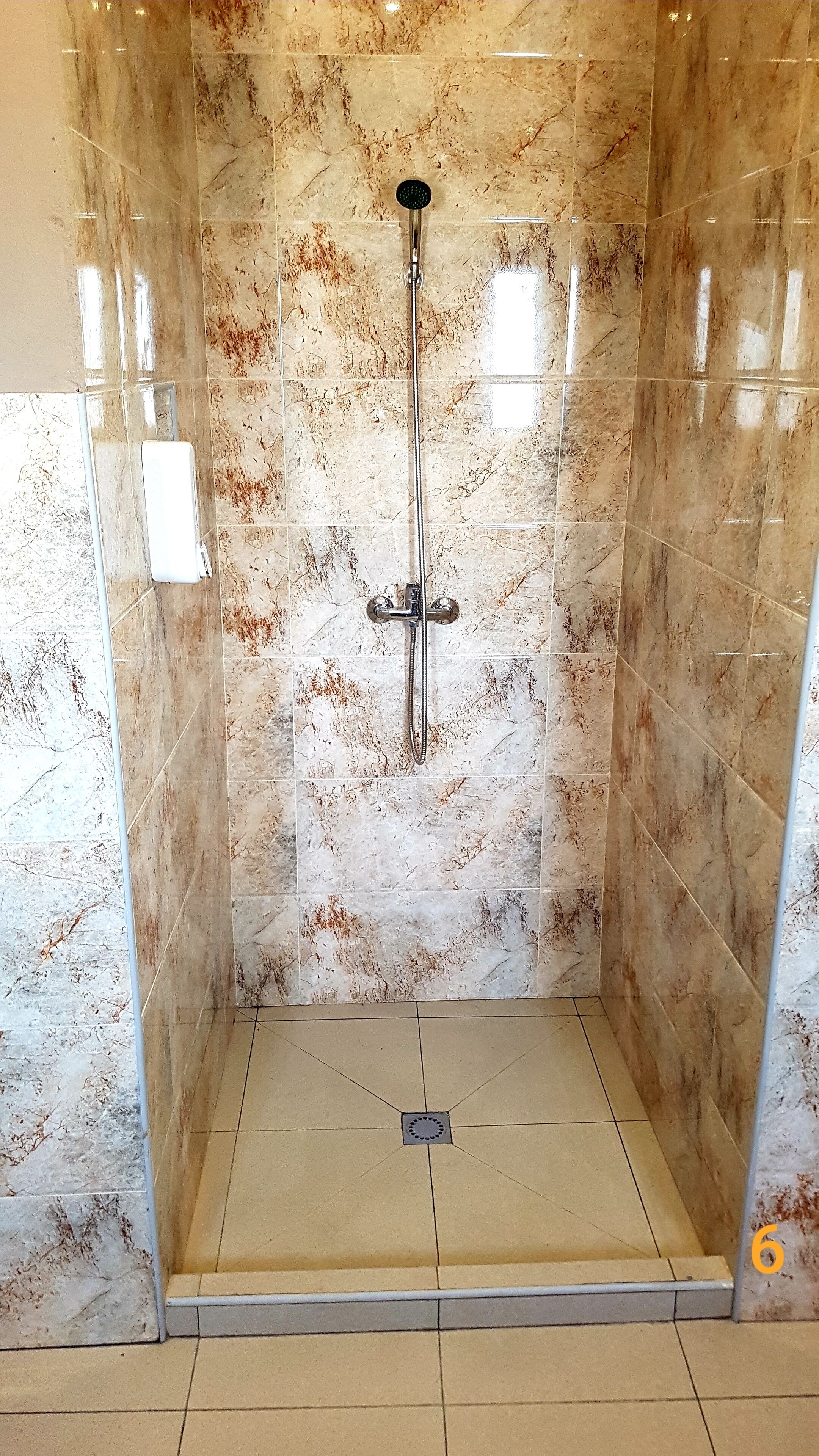 A shower enclosure with a marble wall and floor, a handheld showerhead, and a drain in the center.
