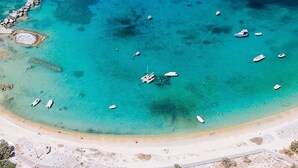 Una vista aerea di una spiaggia con acque cristalline turchesi, imbarcazioni e una riva sabbiosa.