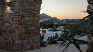 Un arco in pietra conduce a una zona con sedute e cuscini, con vista su una montagna al tramonto.
