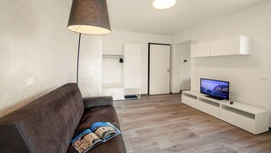 En moderne stue med en sofa, et fjernsyn på et hvidt tv-møbel, og en lampe.